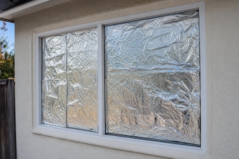 Una ventana de marco blanco en una pared clara con sus cristales totalmente cubiertos por papel de aluminio arrugado.