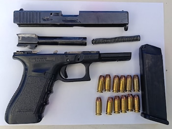 Una pistola negra desmontada en sus componentes, un cargador y doce cartuchos colocados sobre una superficie blanca