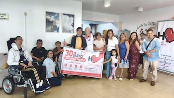 Un grupo de diez personas, incluyendo algunas en sillas de ruedas, sonríe y posa frente a una pancarta blanca que anuncia el '30 de Mayo Esclerosis Múltiple'