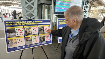 Un hombre señala un cartel de votación interactivo en la estación Jamaica, mostrando opciones de mejora con imágenes de áreas y puntos de colores