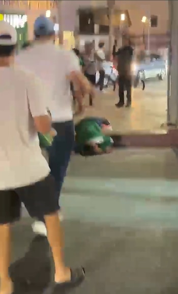 Una persona en el suelo, rodeada por otras personas de pie en una calle iluminada