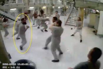 Varios hombres con uniformes claros bailan en un espacio amplio con paredes de celdas y escaleras metálicas. Un óvalo amarillo resalta a un hombre