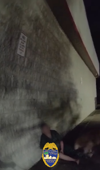 Imagen borrosa y oscura de una persona sentada en el suelo junto a una pared de bloques, con un logo de la policía de Jacksonville superpuesto