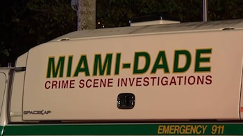 Primer plano de un vehículo blanco de Investigaciones de Escenas del Crimen de Miami-Dade con letras verdes y rojas. Se lee 'MIAMI-DADE CRIME SCENE INVESTIGATIONS' y 'EMERGENCY 911'