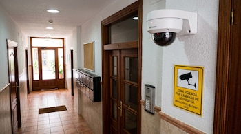 Cámara de seguridad blanca tipo domo con cartel amarillo de aviso, buzones y puerta de madera en el pasillo de un edificio.