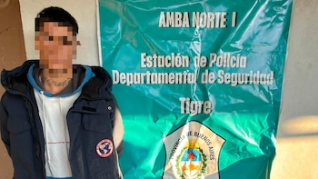 Un hombre con el rostro pixelado, con tatuaje en el cuello que dice 'Rodolfo' y una chaqueta oscura, parado frente a un cartel verde de la Estación de Policía de Tigre