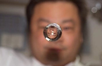 Una esfera de agua flotante refleja de forma invertida el rostro de un hombre, cuya cara aparece desenfocada en el fondo