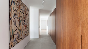 Vista de un pasillo moderno con un gran tapiz abstracto multicolor en la pared izquierda, armarios de madera en la derecha y suelo de baldosas grises.