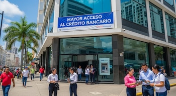 Vista exterior de un edificio de vidrio con un gran cartel azul "MAYOR ACCESO AL CRÉDITO BANCARIO", con gente caminando en la acera soleada de una ciudad.