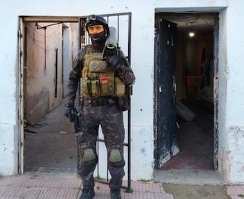 Un agente de seguridad con uniforme de camuflaje, casco, gafas amarillas y chaleco táctico porta un dispositivo cilíndrico al hombro y una pistola