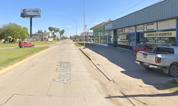 Calle pavimentada Avenida Maipú, edificio comercial azul y verde, camioneta plateada, coche rojo, cartel publicitario, cielo azul despejado, árboles y palmeras