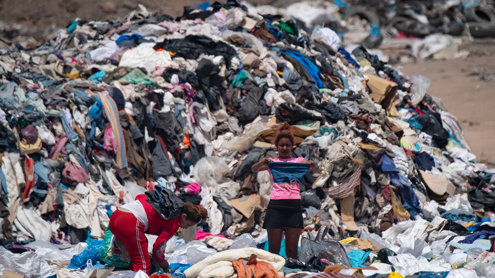 Mujeres buscan ropa usada entre toneladas de prendas desechadas en el desierto de Atacama, en Alto Hospicio, Iquique, Chile, el 26 de septiembre de 2021.(MARTIN BERNETTI / AFP)