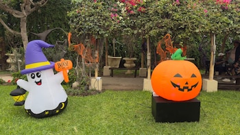 Figuras inflables de un fantasma con sombrero y una calabaza decorativa sobre el césped junto a una pérgola con plantas y adornos anaranjados