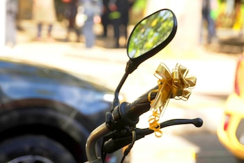 Manillar y espejo retrovisor de un escúter con un lazo dorado atado a la empuñadura