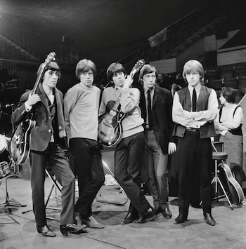 Fotografía en blanco y negro de The Rolling Stones, cinco jóvenes posando en un escenario con guitarras eléctricas y de bajo