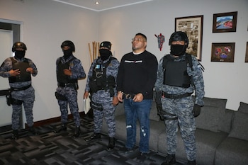 Un hombre esposado junto a cuatro agentes con uniforme táctico y el rostro cubierto en una sala con sillones y cuadros