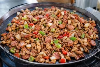 Carne picada, rodajas de salchicha, pimientos rojos y verdes y trozos de cebolla sobre un disco metálico cóncavo.