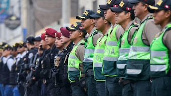 Una fila de hombres policías con gorras negras, uniformes beige y chalecos verdes reflectantes. Algunos visten uniformes negros y boinas rojas