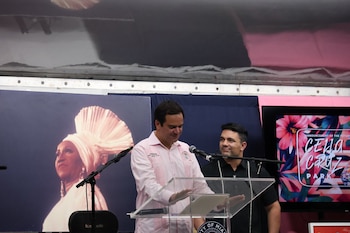 Un hombre habla en un atril oficial flanqueado por otro hombre, un retrato de Celia Cruz y una pantalla sobre el futuro parque Celia Cruz