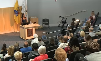 Una mujer habla desde un podio de Camden County College ante un público sentado en las butacas de un auditorio