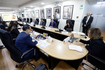 Autoridades gubernamentales sentadas alrededor de una gran mesa de conferencias con computadoras portátiles y letreros de nombres