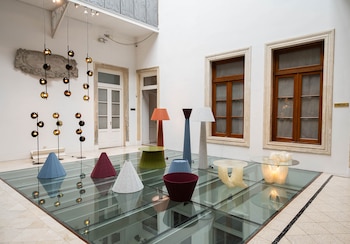 Lámparas de pie, pantallas cónicas y mesas bajas dispuestas sobre un piso de vidrio transparente en un patio interior blanco