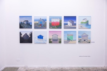 Diez cuadros cuadrados con pinturas de casas en diferentes paisajes están ordenados en dos filas sobre una pared blanca