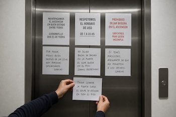 Dos manos sujetan una nota impresa frente a la puerta metálica de un ascensor llena de carteles impresos y notas manuscritas.