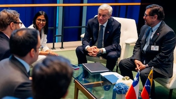 Seis personas con ropa formal conversan en torno a una mesa con pequeñas banderas de Chile y Venezuela