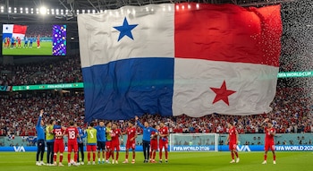 Jugadores de fútbol celebran en un estadio. Detrás, una enorme bandera de Panamá con el cuadro azul abajo a la izquierda ondea mientras cae confeti.