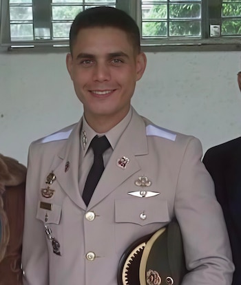 Retrato de un hombre con uniforme militar beige, corbata negra e insignias en el pecho que sostiene una gorra de plato bajo el brazo