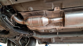 Parte inferior de un coche mostrando un catalizador, tubos de escape, silenciador, chasis, suspensión, un neumático y elementos de la dirección.