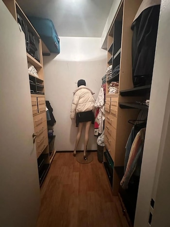 Vestidor con estantes de madera y cajones en ambos lados. Un maniquí con chaqueta blanca y falda negra se ubica en el centro. Suelo de madera