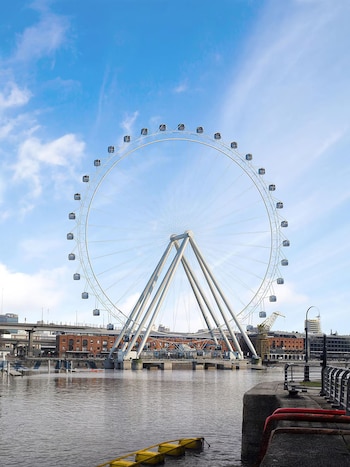 Gran noria blanca con cabinas sobre el agua de los diques de Puerto Madero, con edificios y un puente de fondo bajo un cielo azul claro
