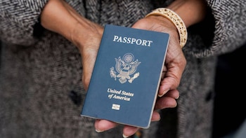 Primer plano de una persona sosteniendo un pasaporte azul de los Estados Unidos. Se ven las manos y parte de una chaqueta texturizada