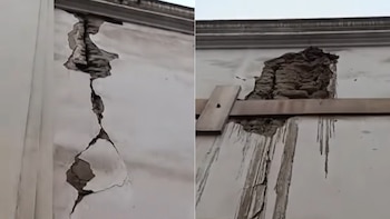 Primer plano de una pared exterior blanca con una gran grieta vertical que expone mampostería interna, reforzada con tablas de madera horizontales