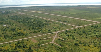 Vista aérea de una pista de aterrizaje de concreto con calles de rodaje rodeadas por campos verdes cerca de una masa de agua