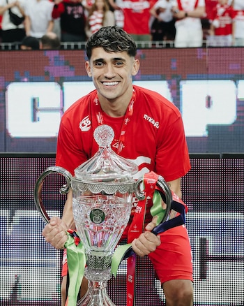 Primer plano de Pablo Solari, sonriendo y sosteniendo un gran trofeo de cristal y metal, adornado con cintas rojas y verdes, en un estadio