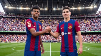 Dos futbolistas jóvenes con camiseta del FC Barcelona se estrechan las manos en el césped de un estadio con público.