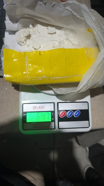 Una balanza digital marca 647 gramos bajo una bolsa con un paquete de cinta amarilla abierto que contiene sustancia blanca