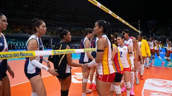 Jugadoras de voleibol vestidas con uniformes deportivos estrechan sus manos por debajo de una red en una cancha cubierta.