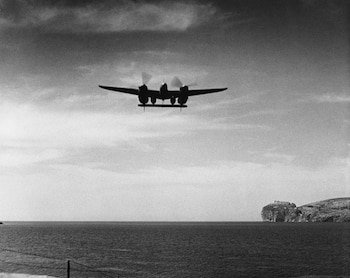 Un avión P-38 Lightning de doble cola y dos motores vuela a baja altitud sobre el mar, con acantilados y un faro a la derecha