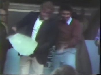 Imagen borrosa de dos hombres, uno rubio y otro con bigote, que manipulan un gran bloque translúcido. Un tercer hombre de gafas está a la izquierda