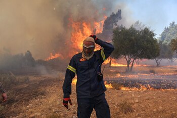 Un bombero camina junto a las llamas que se elevan mientras un incendio forestal arde cerca del pueblo de Vati