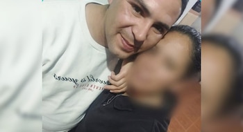 Un hombre con camiseta blanca impreso con texto junto a una persona cuyo rostro está borroso