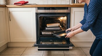 Una mujer introduce una bandeja de metal en un horno abierto que contiene varios moldes y recipientes.