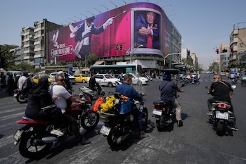 Vehículos pasan junto a una valla publicitaria que muestra al presidente estadounidense Donald Trump junto a un mago y las palabras "¡No trucos! ¡Parpadea, te has ido", en el centro de Teherán, Irán, lunes 31 de agosto de 2026. (Foto AP/Vahid Salemi)