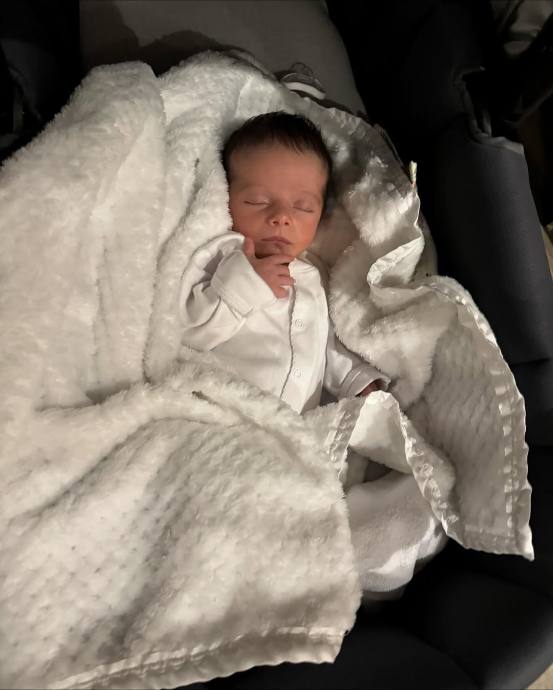 A poco tiempo de su llegada a la familia, el bebé arropado por completo entre mantas blancas y un pijama del mismo color