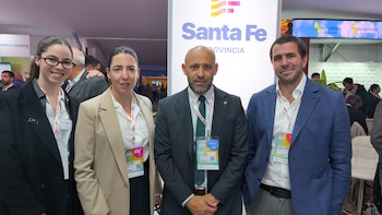 Cuatro personas con vestimenta formal y credenciales identificatorias posan frente a un panel con el logotipo de la provincia de Santa Fe