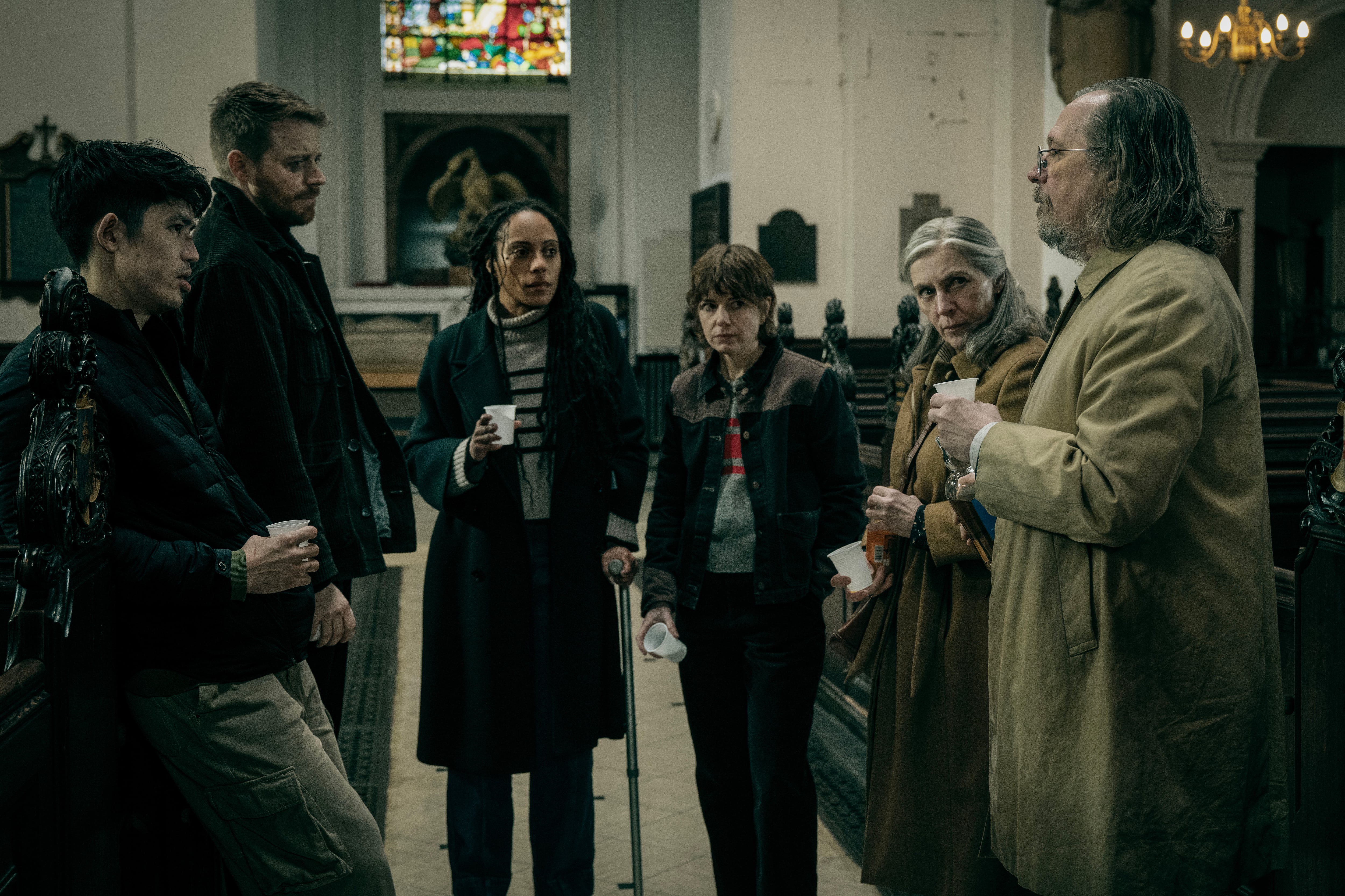 Gary Oldman, Rosalind Eleazar y Christopher Chung conversan en el interior de una iglesia durante una escena de la sexta temporada de